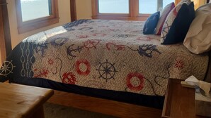 Ein Schlafzimmer mit einem großen Bett, einer hölzernen Bank und Seeblick durch drei Fenster.