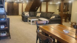 Ein gemütliches Wohnzimmer mit einer Couch, einem Couchtisch und einem Holzesstisch. Eine Treppe führt auf eine erhöhte Ebene.