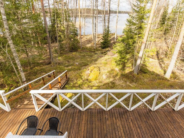 A wooden deck with a railing overlooking a forested area and a lake.