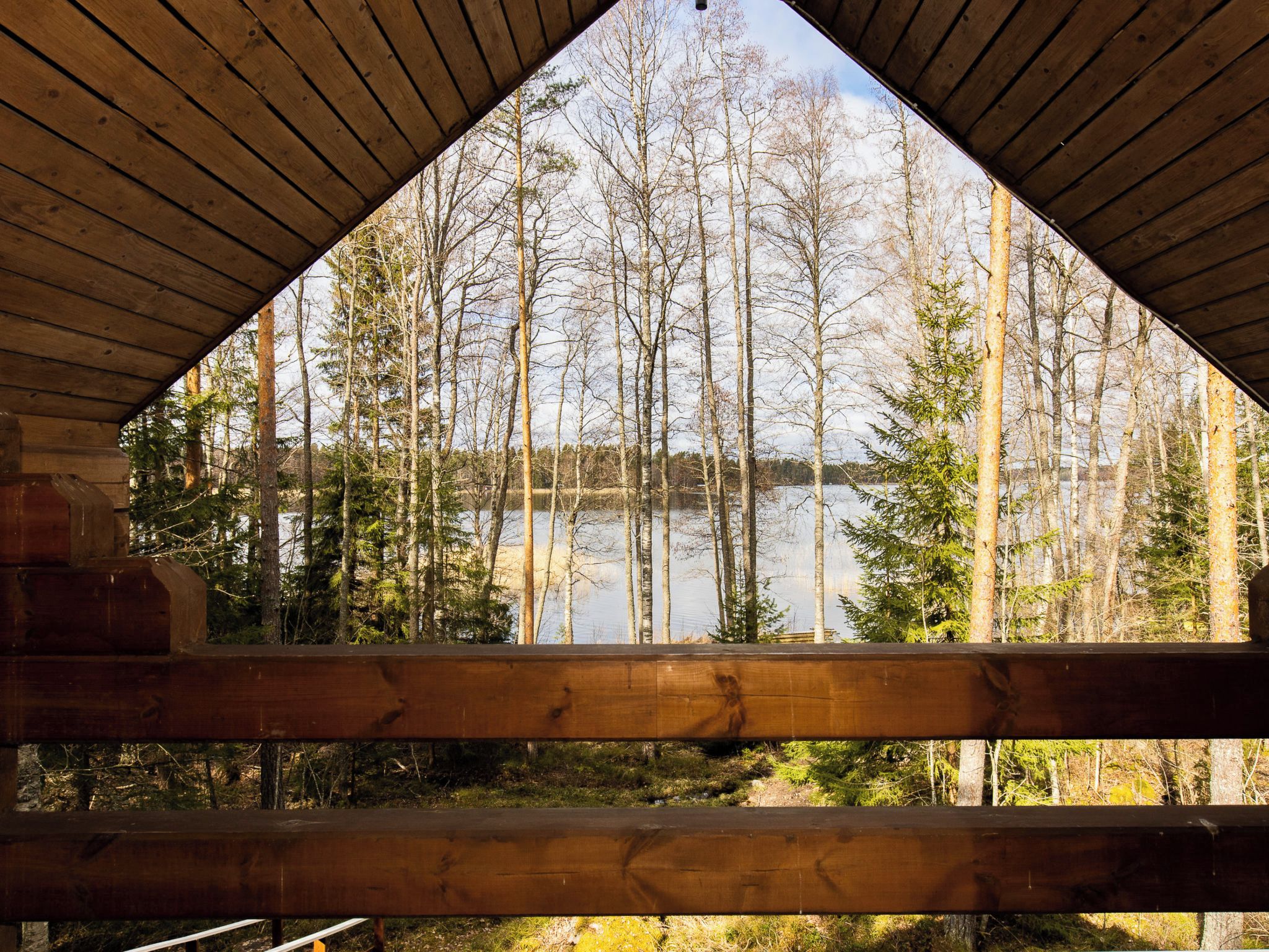 A wooden cabin with a triangular roof and a view of a forest and lake.