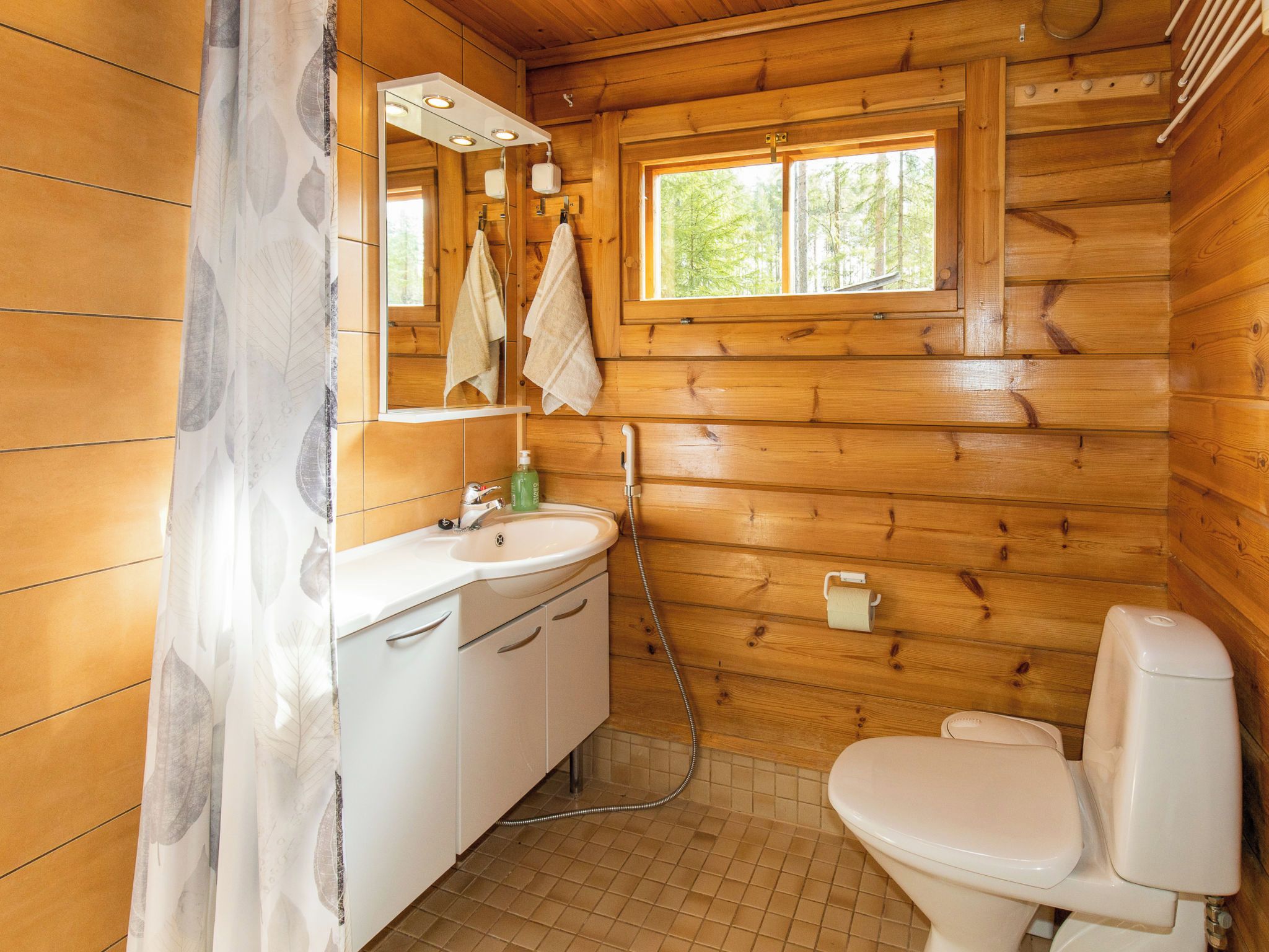 Baño de cabaña de madera con lavamanos, espejo, toallero y retrete.
