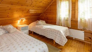 A cozy wooden cabin bedroom with two single beds, a nightstand, and a window with curtains.