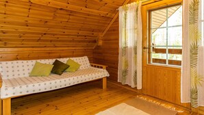 A cozy wooden cabin room with a sofa, a window with curtains, and a wooden ceiling.
