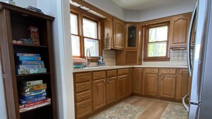 A kitchen with wooden cabinets, a refrigerator, and a game shelf. - Douglas Lake House: Summer Days Made for Swimming, Kayaking, and Starry Nights (Levering)