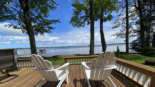 A wooden deck with two Adirondack chairs facing a lake, a grill, and a bench. - Douglas Lake House: Summer Days Made for Swimming, Kayaking, and Starry Nights (Levering)