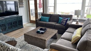 A living room with a television, a sofa, a coffee table, and a view of a lake. - Douglas Lake House: Summer Days Made for Swimming, Kayaking, and Starry Nights (Levering)