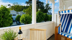 Een balkon met een houten stoel, een gestreepte bank, een tafel met een fles en glas, en een bloempot.
