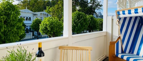 A balcony with a wooden chair, a striped sofa, a table with a bottle and glass, and a potted plant.