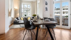 Een eetgedeelte met een tafel, stoelen en een uitzicht op gebouwen door grote ramen.
