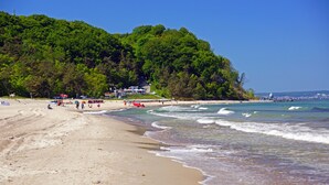 Een strand met een bebost heuveltje, heldere lucht en enkele mensen.
