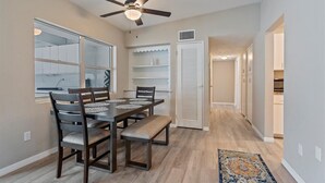 A dining area with a wooden table and chairs, a ceiling fan, and a view into the kitchen. - Florida Living (Bradenton)