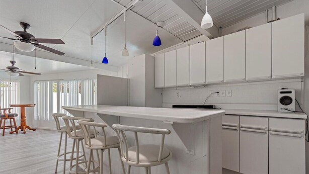 A modern kitchen with white cabinets, a central island with bar stools, pendant lights, and ceiling fans. - Florida Living (Bradenton)