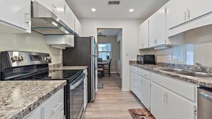 A modern kitchen with granite countertops, stainless steel appliances, and white cabinetry. - Florida Living (Bradenton)