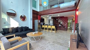 A modern living area with a sofa, chairs, a coffee table, and a kitchen in the background.