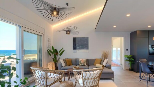 Un moderno salón con un gran ventanal que da a un balcón, mobiliario de mimbre e iluminación contemporánea.
