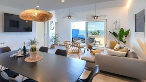Una sala de estar moderna con comedor, ventanas amplias con vista al mar y un televisor de pantalla plana montado en la pared.