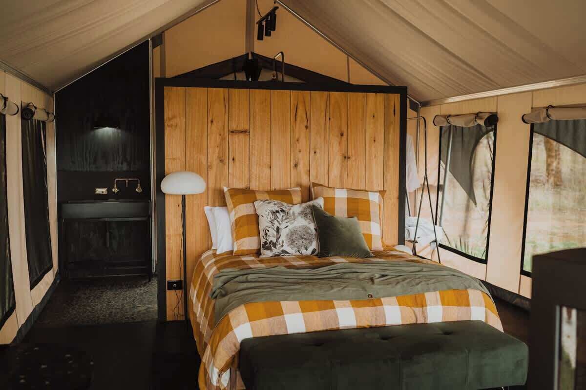 A cozy bedroom with a checkered bedspread, a wooden headboard, a bedside table, and a hanging light fixture.
