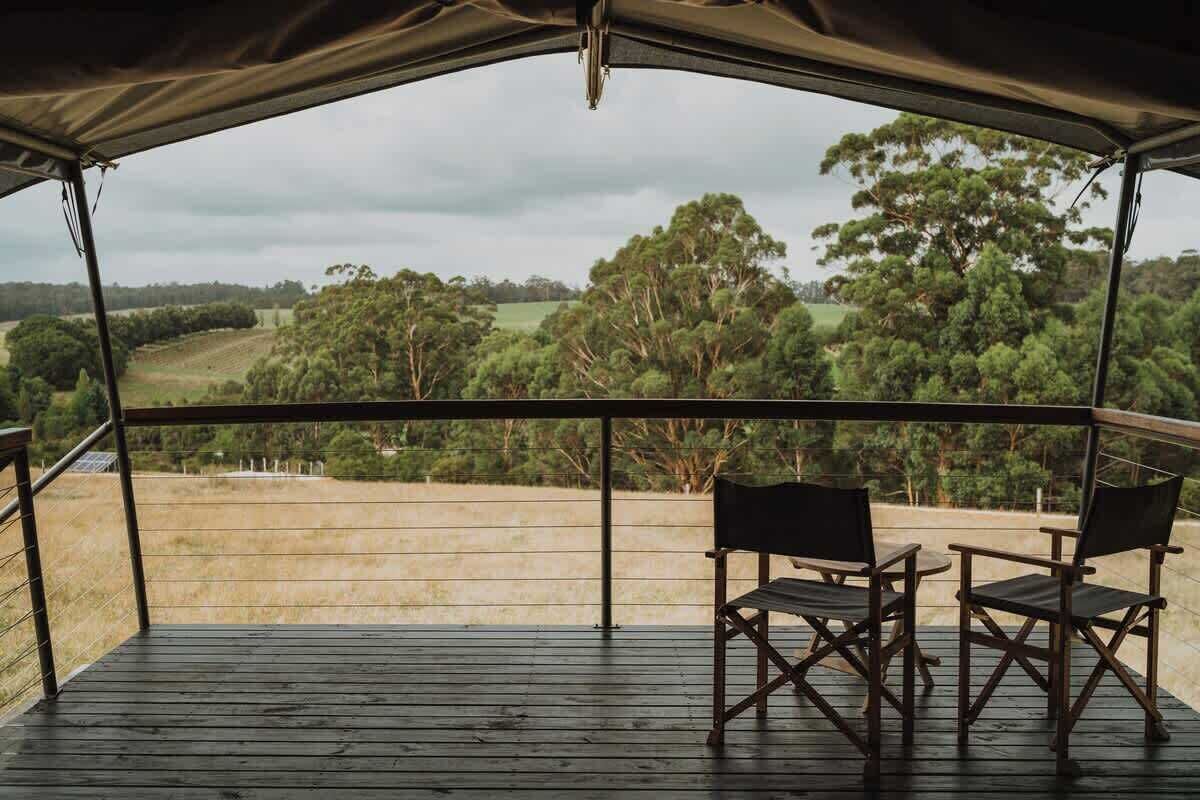 A covered outdoor area with a wooden deck, two chairs, and a view of a green landscape.