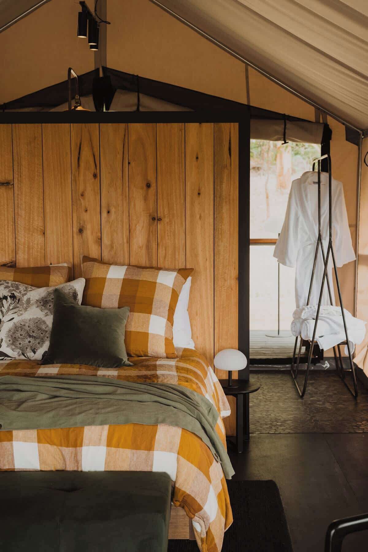 A tented accommodation room with a bed, pillows, a small table, and a hanging chair.