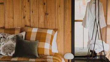 A tented accommodation room with a bed, pillows, a small table, and a hanging chair.