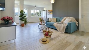 En rummelig opholdsstue med sofa, TV og spisebord. Stueplanter og en hat ligger på gulvet.