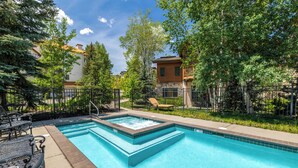 A rectangular pool with a hot tub, surrounded by lounge chairs and a fence.