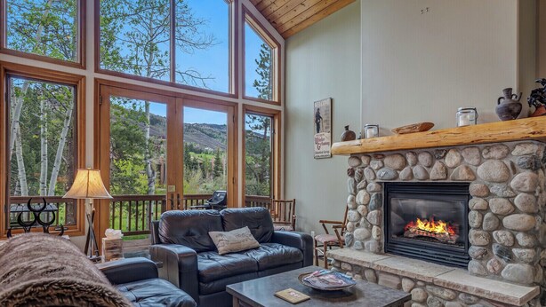 A cozy living room with a stone fireplace, leather sofas, and large windows offering a scenic view.