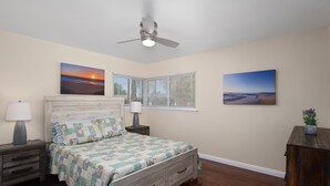 Una camera da letto con un letto di legno, due comodini con lampade, un ventilatore a soffitto e due quadri appesi al muro.