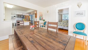 A dining area with a wooden table and chairs, a kitchen in the background, and a bedroom with a bed and window. - Yellow Cottage in Lake Chelan (Chelan)