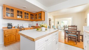 A kitchen with wooden cabinets, a white countertop, and a dining area with a wooden table and chairs. - Yellow Cottage in Lake Chelan (Chelan)