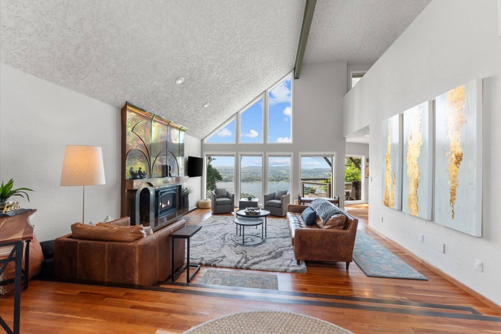 Un salón amplio con chimenea, sofás de cuero, una mesa de centro y grandes ventanales con vistas al exterior.