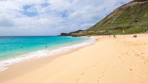 A beach with clear turquoise water, sandy shore, and a grassy hill in the background. - Waterfront Spacious Home near Beach & Hiking. Family Friendly w/Boat Dock & Pool (Honolulu)