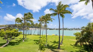 A tropical landscape with palm trees, a grassy area, and a view of the sea. - Waterfront Spacious Home near Beach & Hiking. Family Friendly w/Boat Dock & Pool (Honolulu)