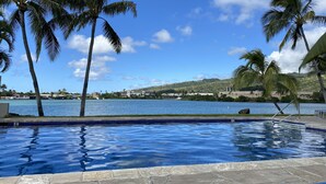 A swimming pool with palm trees and a view of a body of water and distant hills. - Waterfront Spacious Home near Beach & Hiking. Family Friendly w/Boat Dock & Pool (Honolulu)