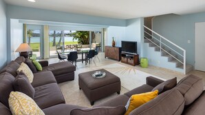 A living room with a large sectional sofa, a dining area with a table and chairs, a television, and a staircase. - Waterfront Spacious Home near Beach & Hiking. Family Friendly w/Boat Dock & Pool (Honolulu)