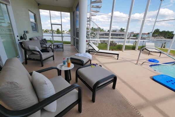 A sunlit outdoor seating area with a pool, lounge chairs, and a view of a body of water and buildings.