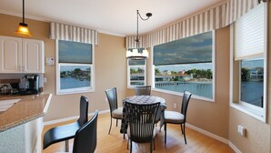A dining area with a round table, chairs, and a view of a body of water through large windows. - Seascape - WHOLE HOUSE 360 water views, pool, gulf (Hernando Beach)