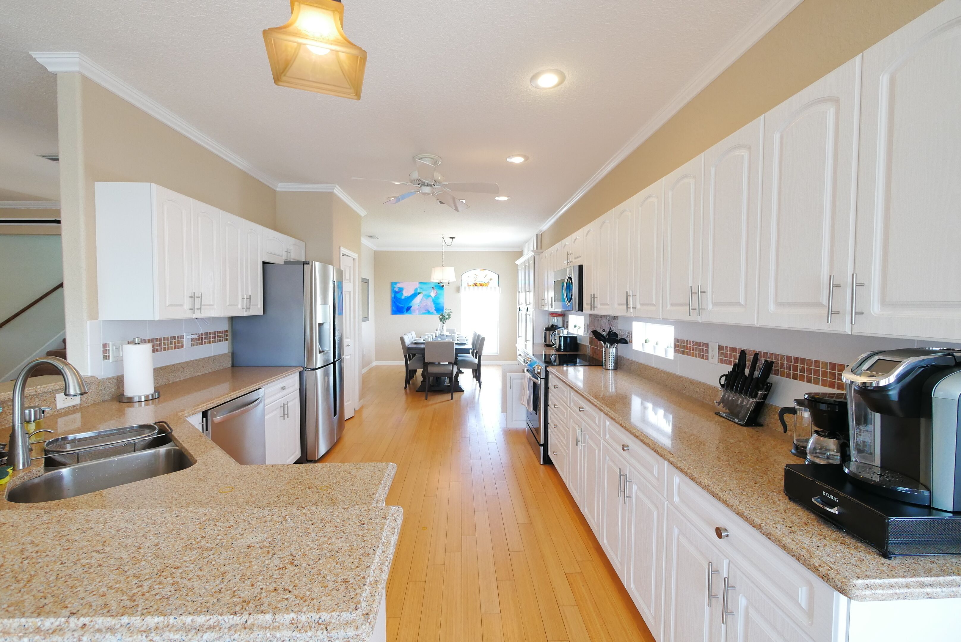 A modern kitchen with white cabinets, granite countertops, stainless steel appliances, and a dining area in the background.