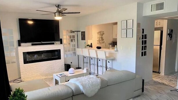 A modern living room with a large TV, a fireplace, a sofa, and a kitchen area with a bar. - VACATION RENTAL!!! (North Fort Myers)