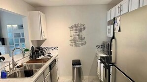 A modern kitchen with stainless steel appliances, a tiled backsplash, and a black trash bin. - VACATION RENTAL!!! (North Fort Myers)