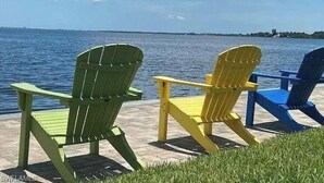 Two Adirondack chairs facing a body of water with a distant shoreline. - VACATION RENTAL!!! (North Fort Myers)