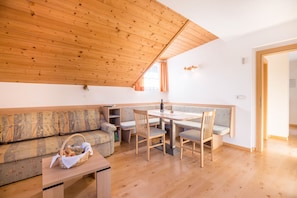 A cozy room with a wooden ceiling, a sofa, a dining table with chairs, and a small table with a basket.