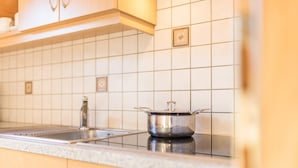 Une cuisine avec un dosseret de carrelage blanc, une casserole en acier inoxydable et des armoires en bois.