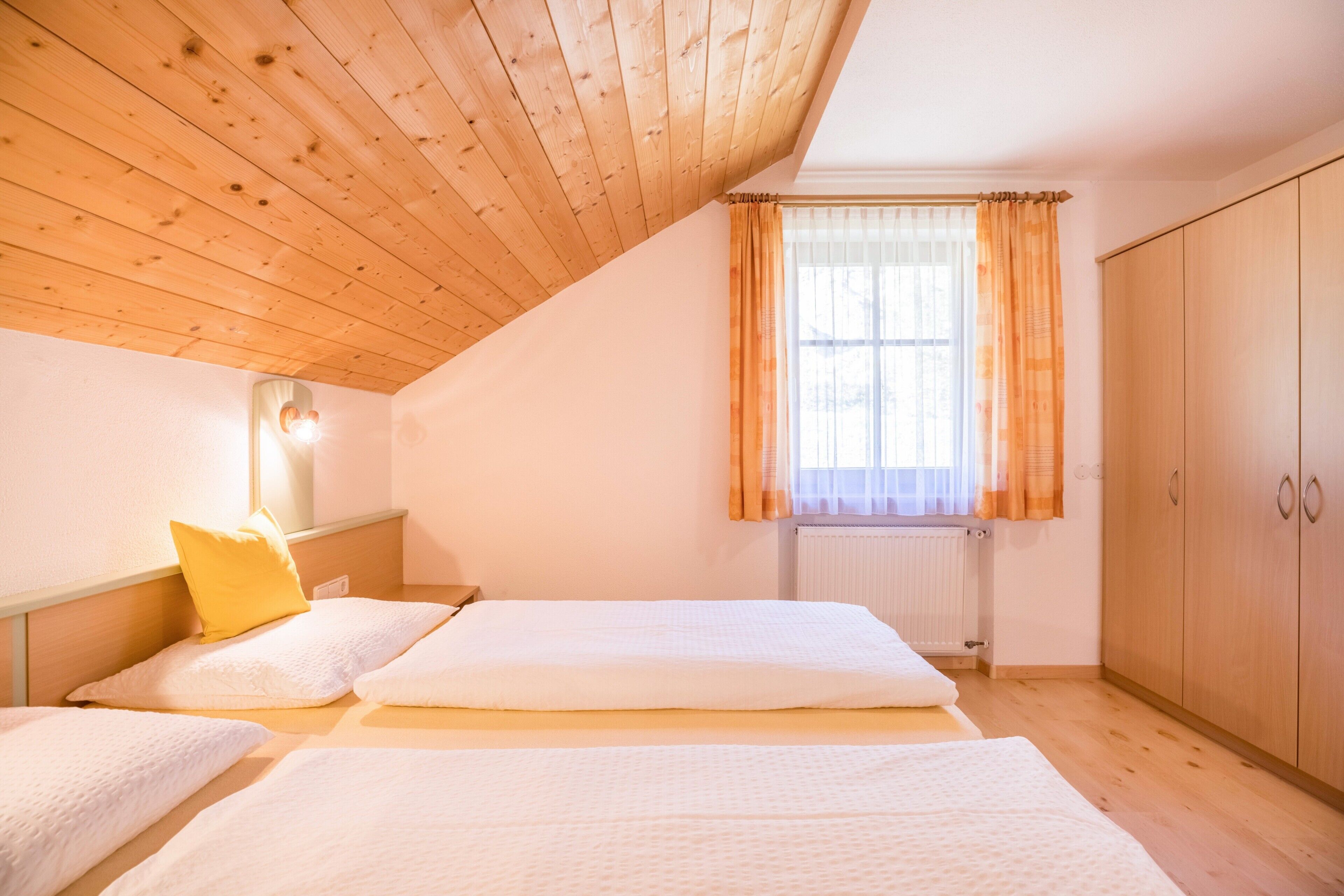 Een slaapkamer met houten balken in het plafond, een raam met gordijnen, een radiator en een kledingkast.