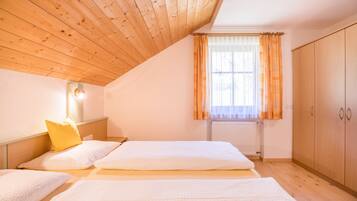 Een slaapkamer met houten balken in het plafond, een raam met gordijnen, een radiator en een kledingkast.