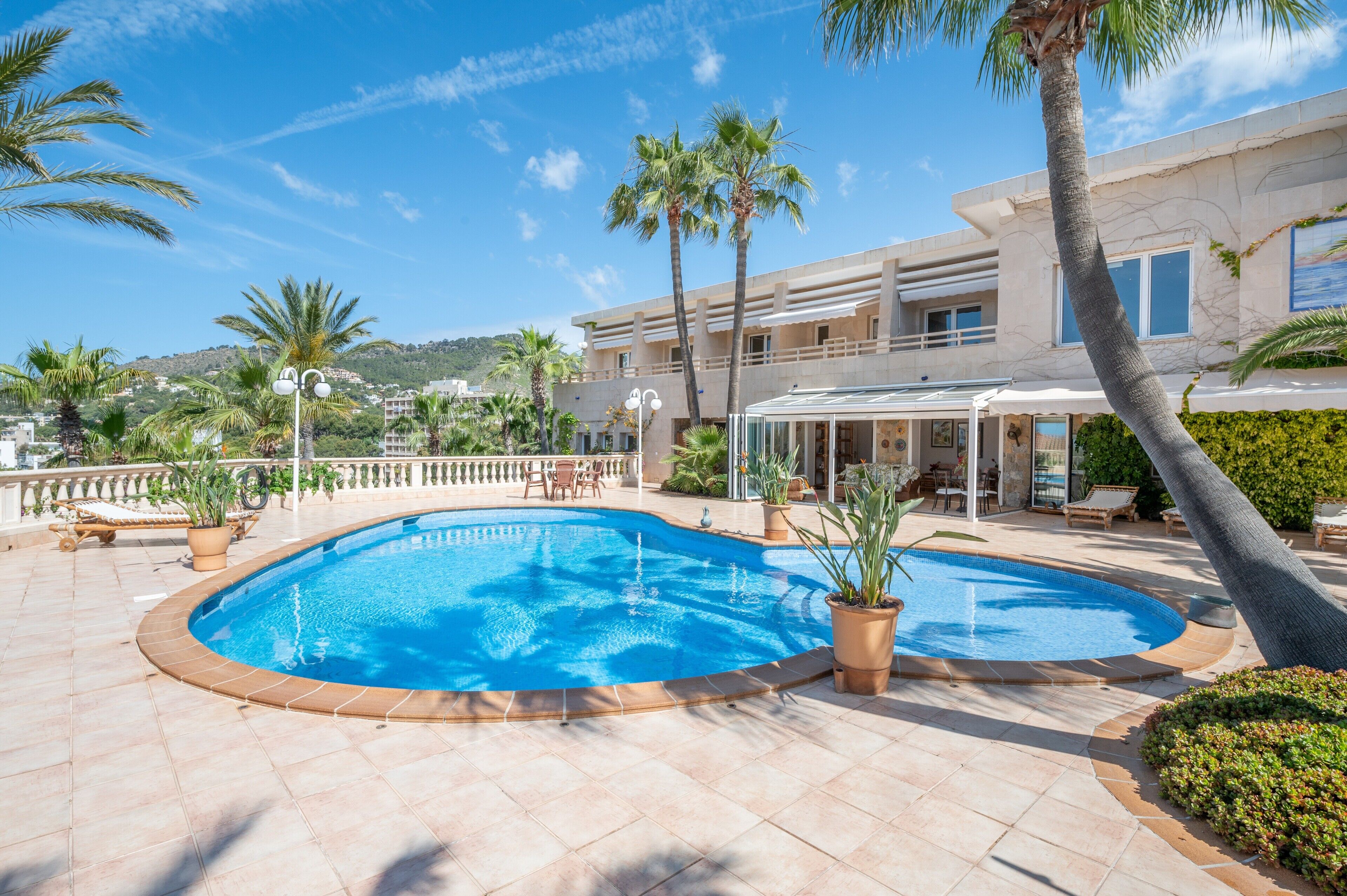 Une piscine avec des chaises longues, des palmiers et un bâtiment doté d’un balcon.