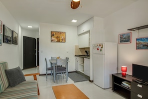 A compact living space with a sofa, dining table, chairs, a kitchen area, and a TV.