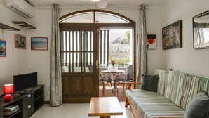 A living room with a sofa, a TV, a table, and a view of the outside.