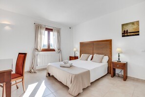 Un dormitorio con una cama grande, dos mesitas de noche, una silla, una ventana con cortinas y un cuadro en la pared.