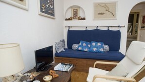 Ett vardagsrum med en blå soffa, vita fåtöljer, ett träbord och en tv.